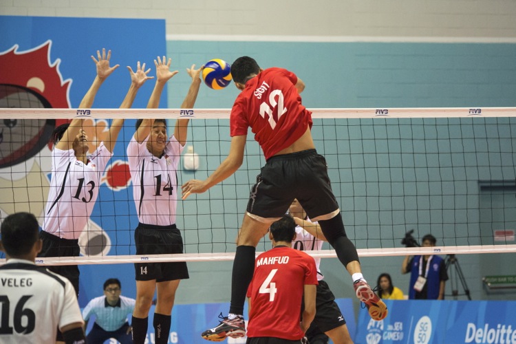 Indonesia’s Ardian Sigit (#12) spikes the ball into the hands of the center  blockers Daryl Lee (#13) and Eng Sin Hau (#14) 