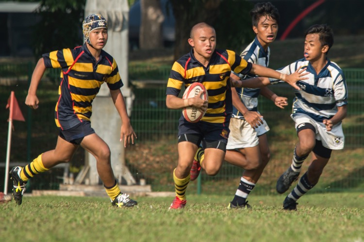 Lim Hongxi (#15) of ACS(I) fends off a tackle from Saints. (Photo © Low Sze Sen/Red Sports)