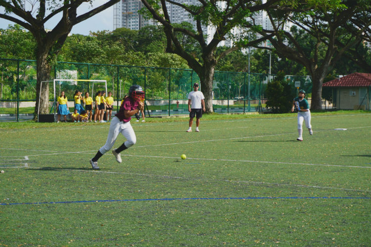 Sakinah (#12) of Tanjong Katong Girls' School advances to first base after making a successful bunt to the Xiao Lian (#99) of Crescent Girls' School during the game of Crescent Girls' School  against Tanjong Katong Girls' School. (Photo 2 by © Pang Chin Yee /REDIntern