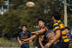 ACS(I)’s Isaac Chow (centre) making a pass, while taking contact, to Independent prop Evan Tan (right). (Photo 2 © Bryan Foo/Red Sports)