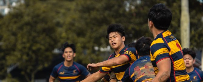 ACS(I)’s Isaac Chow (centre) making a pass, while taking contact, to Independent prop Evan Tan (right). (Photo 2 © Bryan Foo/Red Sports)