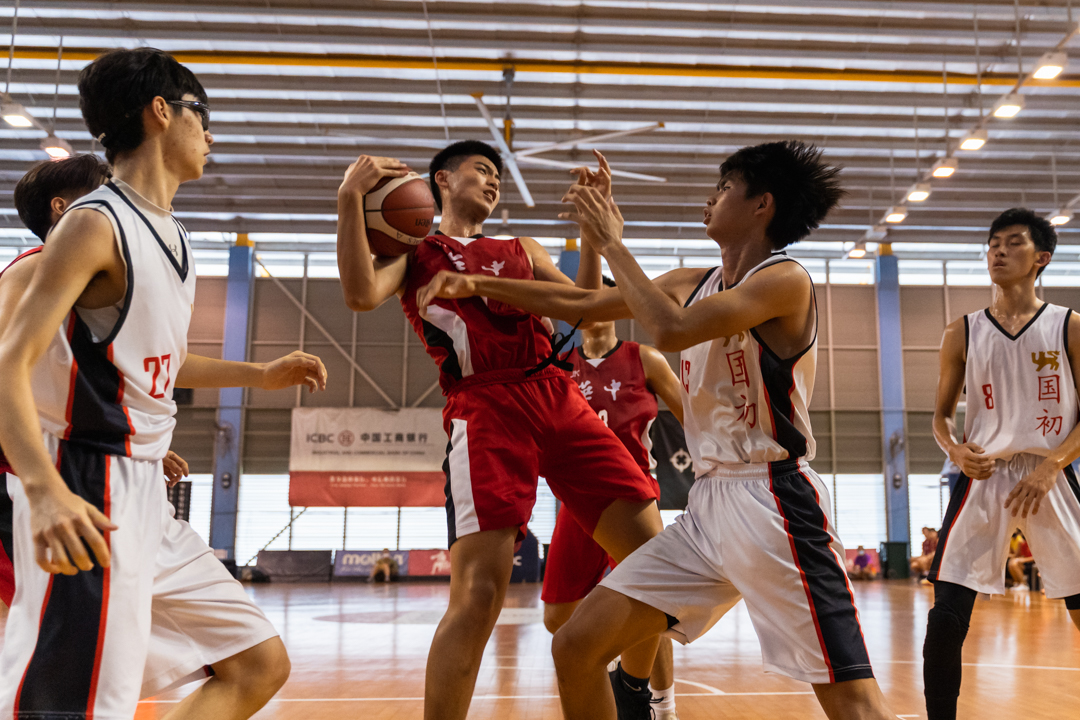 HCI's HCI's Matthew Huang (centre, in red) fends off NJC defenders for the rebound. (Photo X © Bryan Foo/Red Sports)