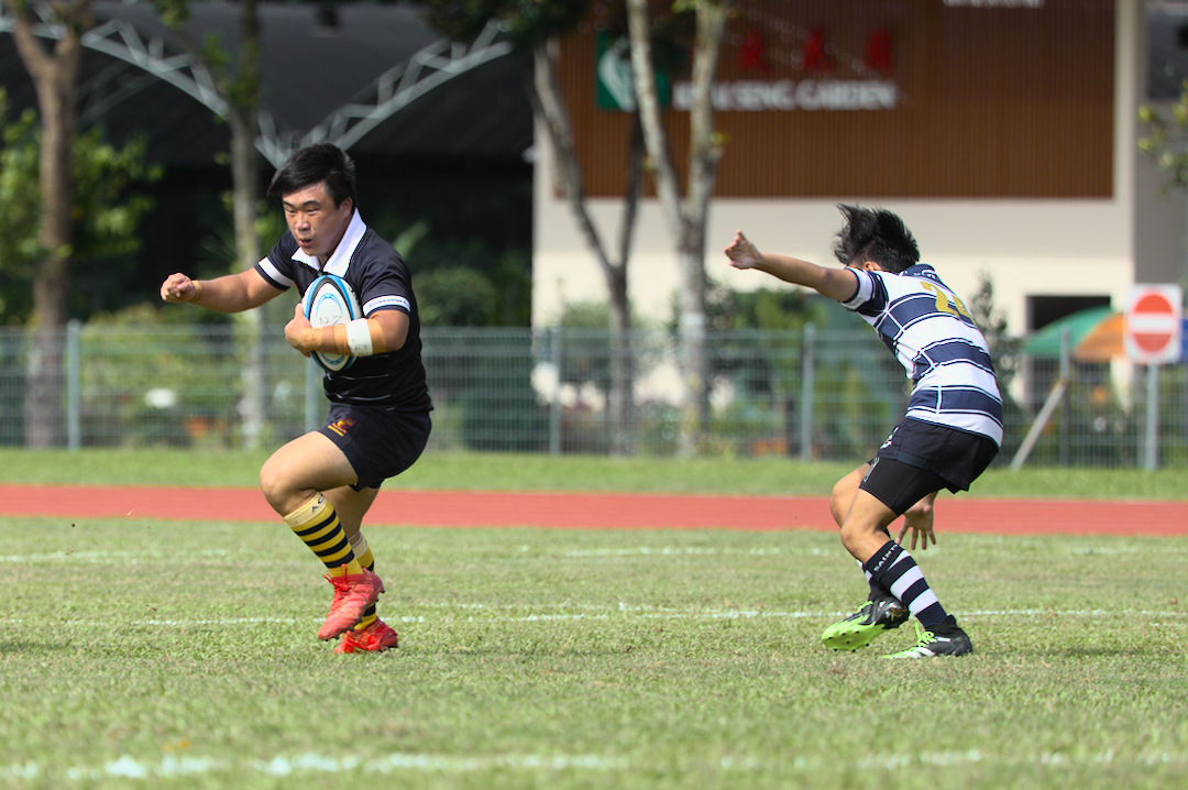 ACJC's Aidan Toh Jing Xiong spins out of the tackle of Saints' Ryan Sing Aik Yong (#24).