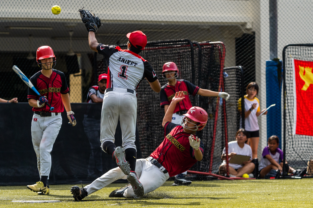 HCI player (centre, bottom) slides towards home plate as NJC pitcher Aniket (NJC #1) tries to catch the ball necessary to tag the HCI runner out. (Photo X © Bryan Foo/Red Sports)