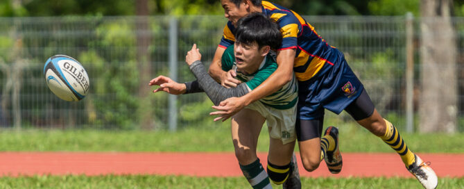 SJI player makes a pass while being tackled by ACS(I) scrumhalf Samuel Lee (AC #9).(Photo X © Bryan Foo/Red Sports)