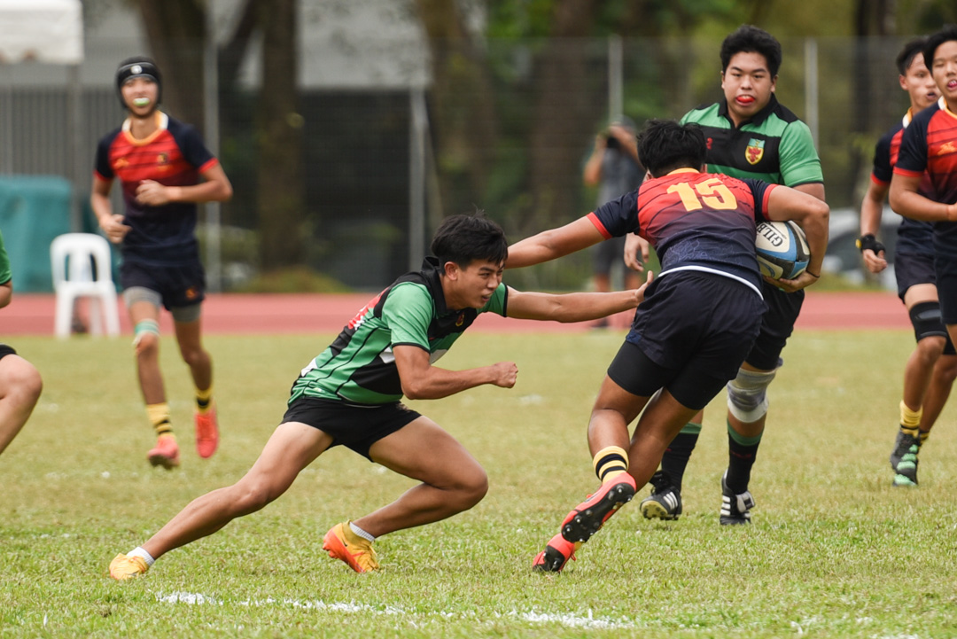 ACJC's Noah Oey attempts to dodge the tackle of RI's Titus Lim (#23). (Photo 18 © Jared Chow/Red Sports)